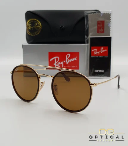 Lunettes de soleil Ray-Ban Round Double Bridge RB3647N dorées avec cerclages en acétate marron et verres marrons B-15, étui noir, boîte grise et livret de garantie chez Optical Gallery.